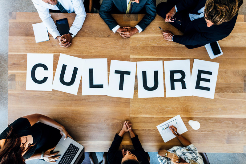 Group of business people with alphabets signs forming the word Culture on table. Top view of business people discussing over work culture in a meeting